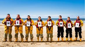 Crew with 'welcome' sign on a beach