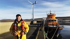 Aith RNLI Mechanic Kevin Henry with the station’s Severn class lifeboat, Charles Lidbury 17-14, and wind turbine in the background