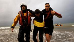 Working together: lifeboat crew member and lifeguard help a swimmer to shore.