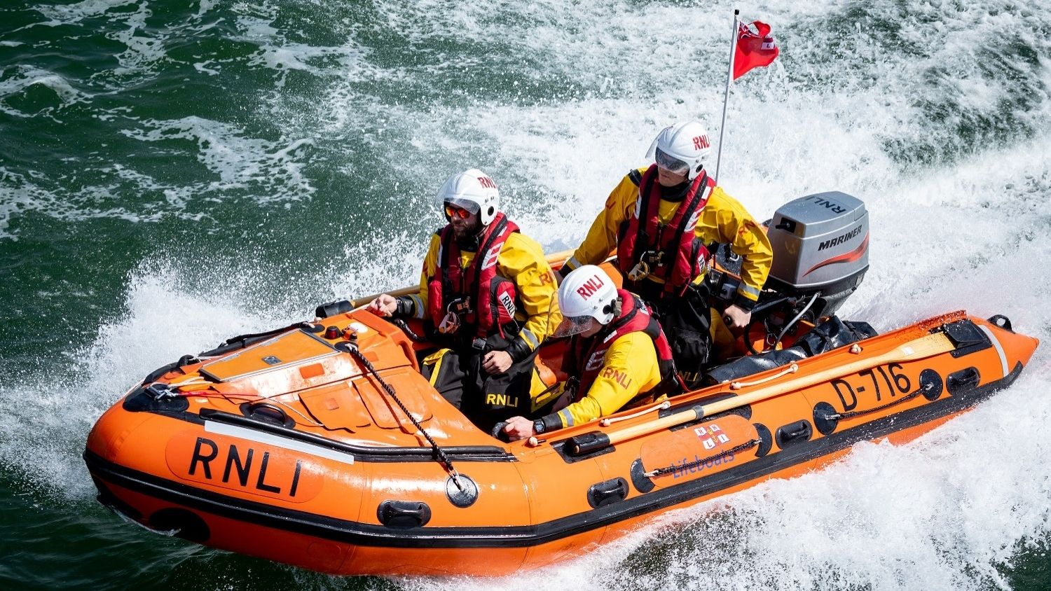 A D class inshore lifeboat is in the sea with three lifeboat crew members onboard.