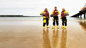 Three crew members standing on the sand next to the Tenby Lifeboat Station slipway.