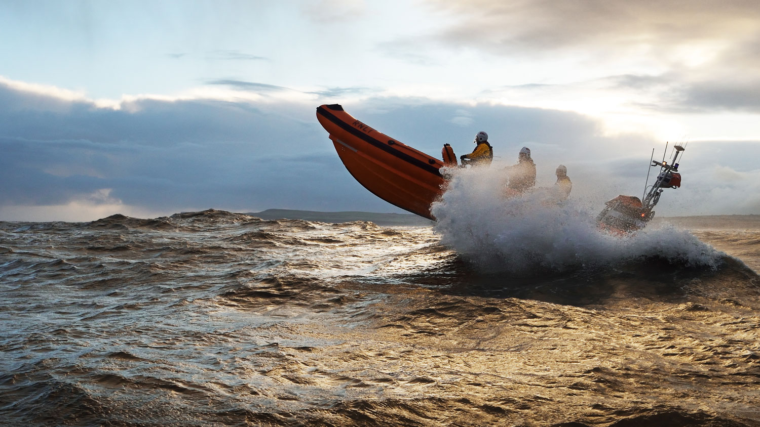 RNLI lifeboat with crew splashing through white horses at sea