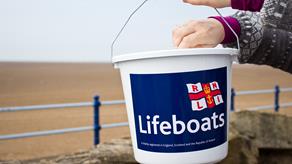 A hand putting money into an RNLI Lifeboats fundraising bucket