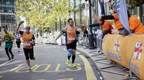 A marathon runner, wearing an orange RNLI vest, high fives his cheering supporters