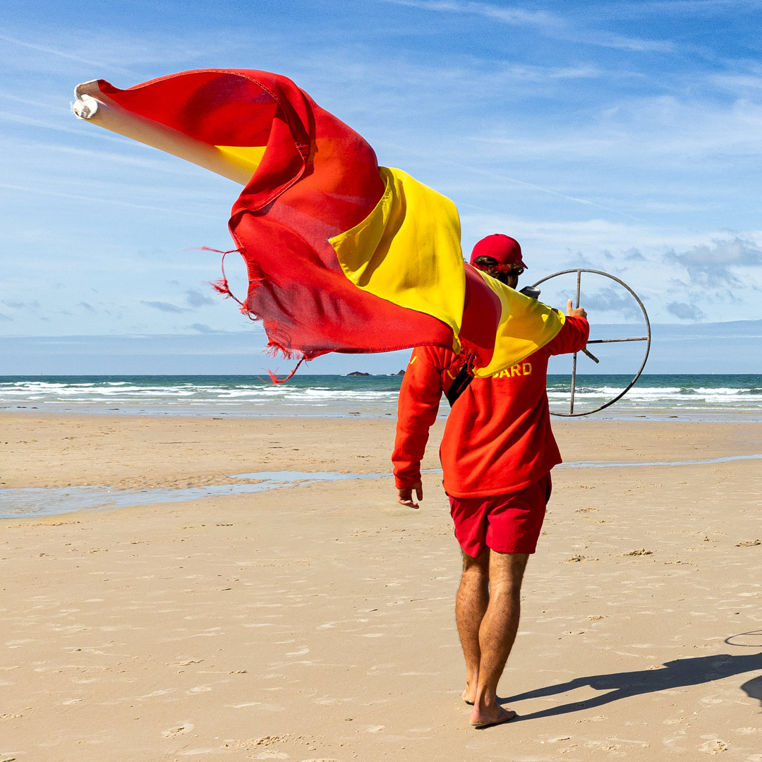 RNLI beach lifeguard carries a red and yellow flag on the beach