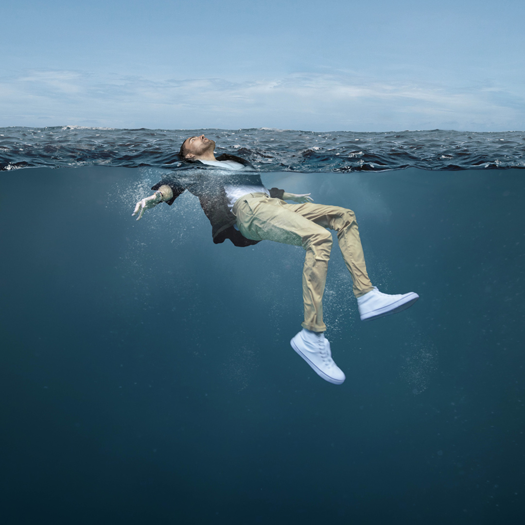 A side view of a fully clothed man floating on his back in the water