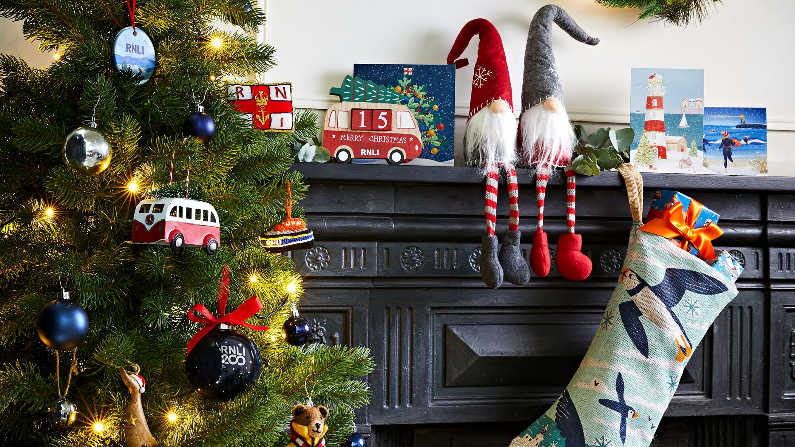 Decorated Christmas tree next to two bearded felt figures and Christmas cards on top of a cast iron fireplace.