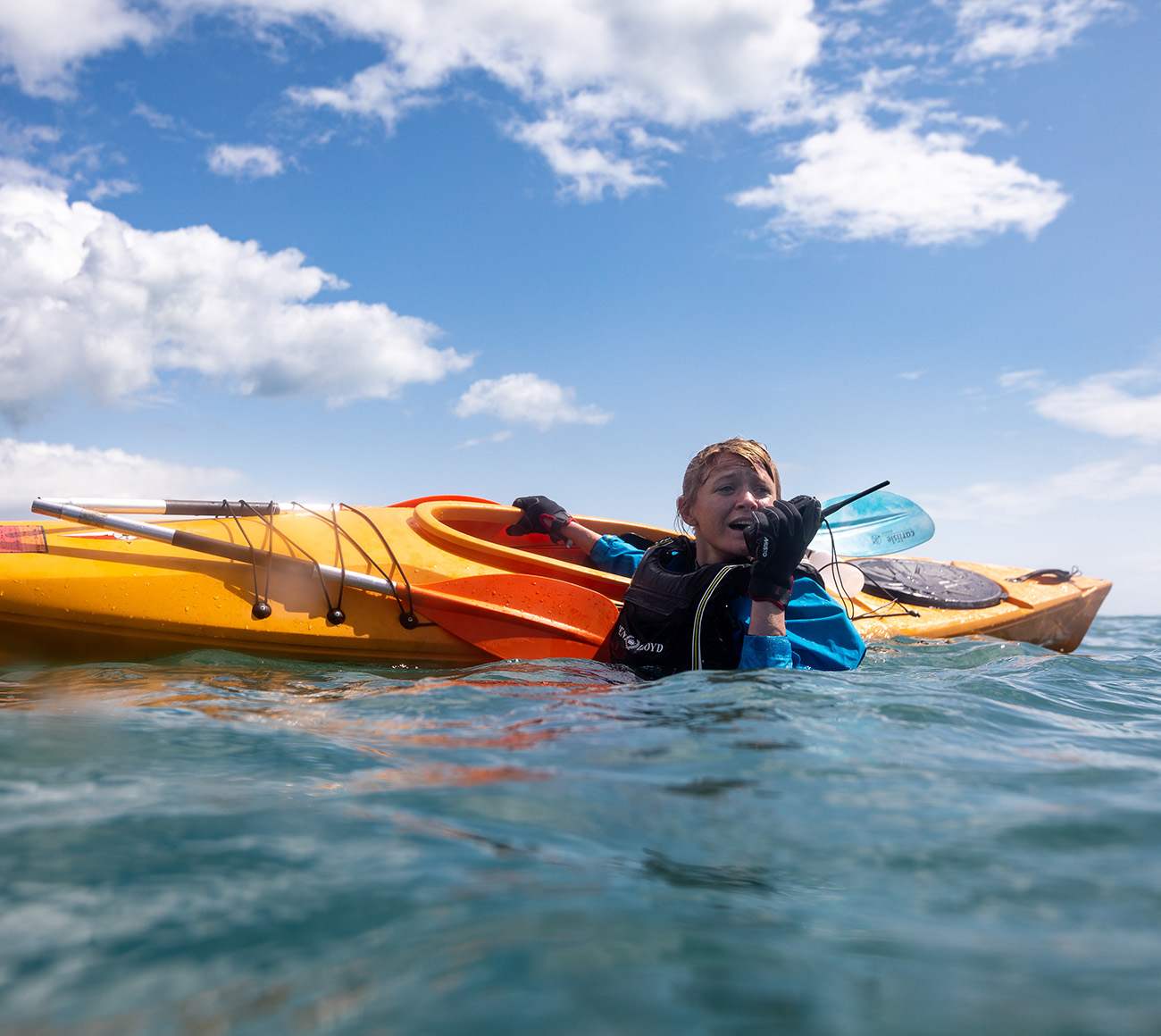 A kayaker is in distress in the water next to her kayak and is talking into a VHF radio