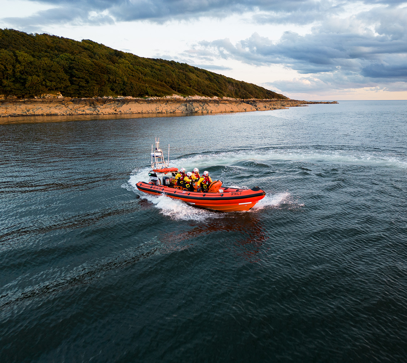 An Atlantic 85 lifeboat with four lifeboat crew members onboard at sea in the evening light, with the beach in the background.