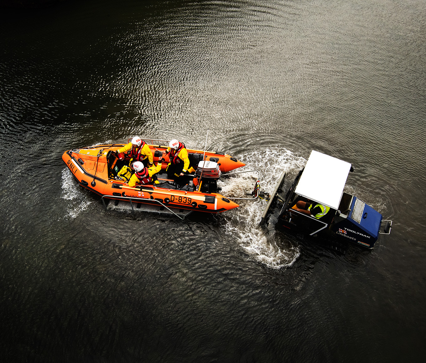 View from above of a D class lifeboat with three lifeboat crew members onboard being launched by a launch vehicle.