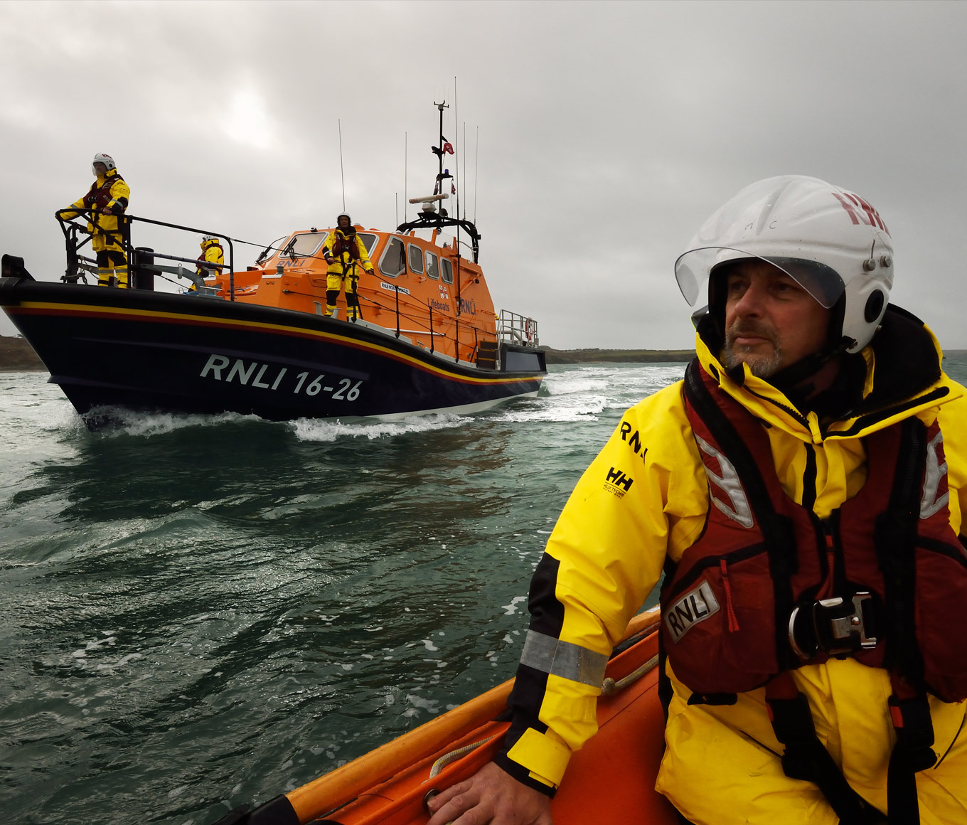 A lifeboat crew member on an XP boat motors on the water in front of a Tamar class lifeboat