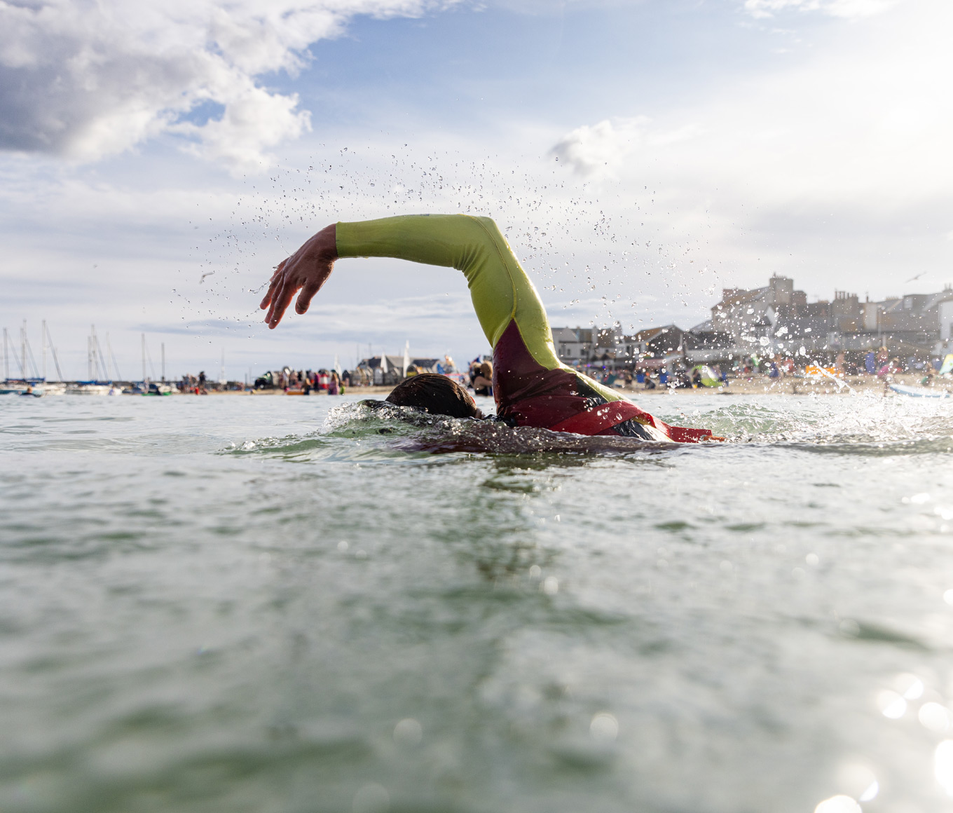 A lifeguard wearing a red and black RNLI wetsuit swims through a calm sea off the coast of West Dorset