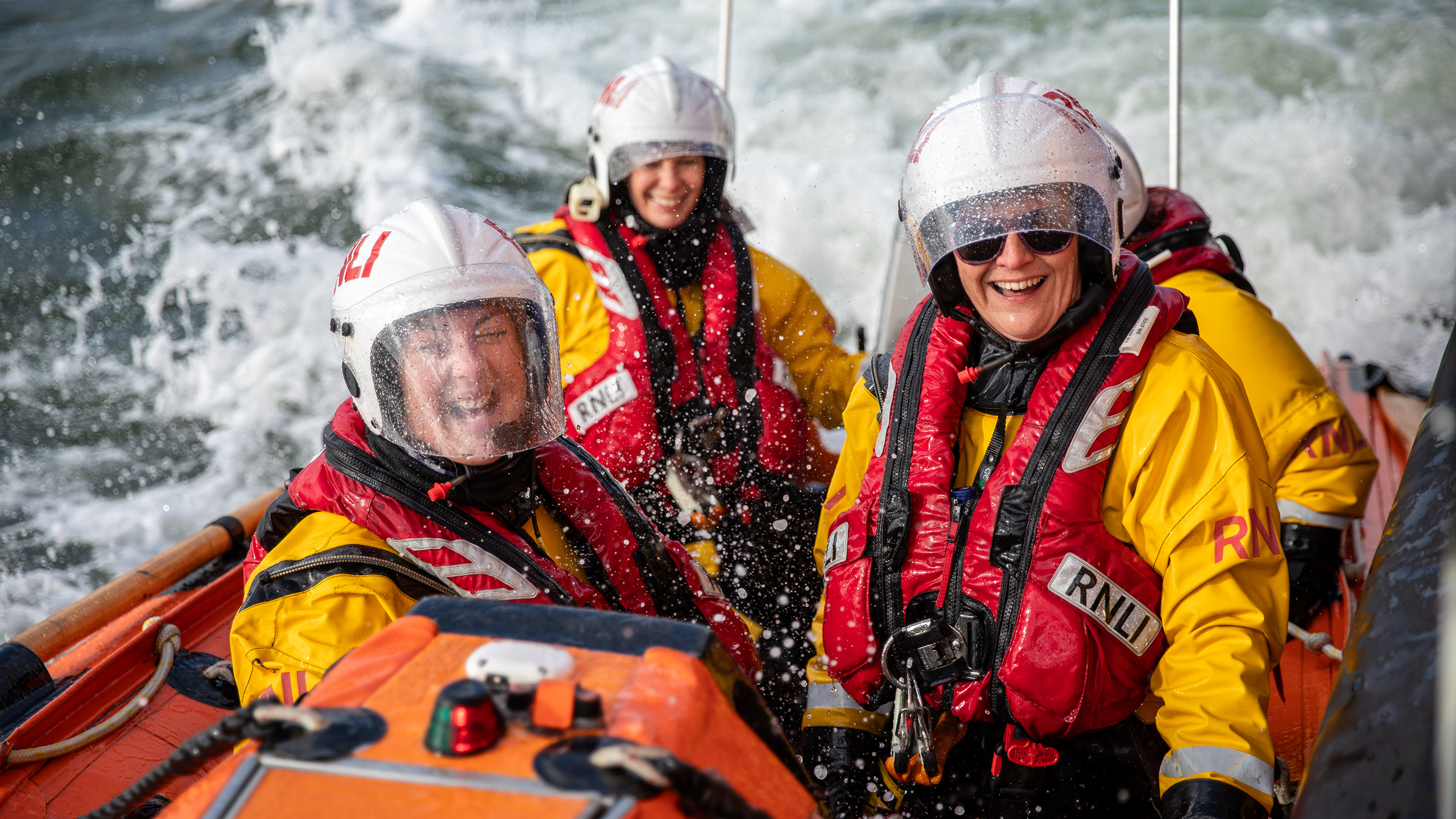 Three female crew members, training on an inshore lifeboat, smile and laugh 