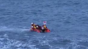 An RNLI inshore D class lifeboat in rough seas with three crew aboard, two lean out to reach for a child in the water on the port side of the lifeboat