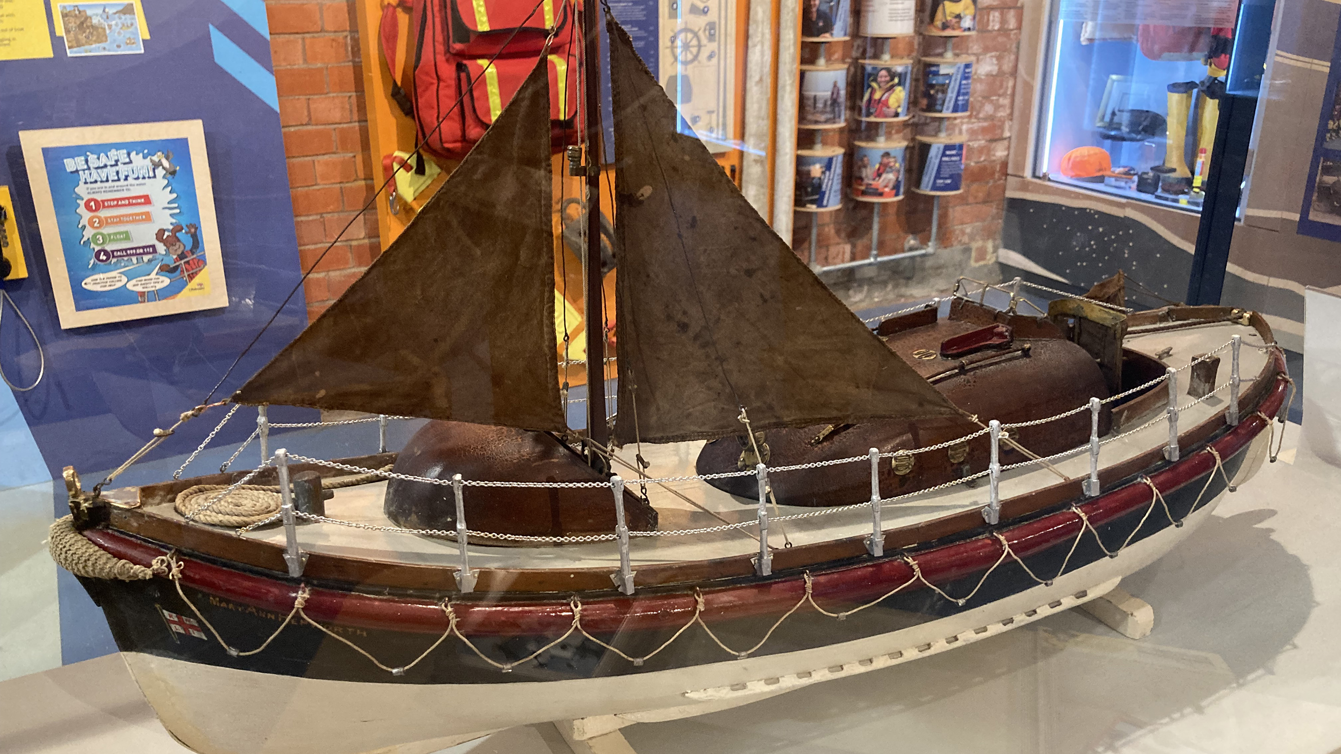 The restored model of the lifeboat Mary Ann Hepworth. It has a painted red, blue and white hull, with brown sails.