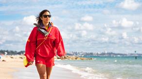A female RNLI lifeguard is walking along the beach on a sunny day.