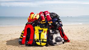 A variety of lifejackets and buoyancy aids piled up on a beach