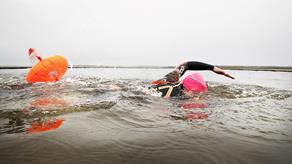 A swimmer wearing a bright pink cap glides through the water, with an orange inflatable tow float bobbing behind her