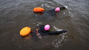 Overhead shot of two open water swimmers, wearing wetsuits and brightly coloured swimming hats, towing brightly coloured swim floats