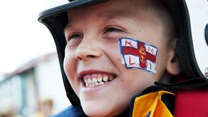 Portrait shot of a young RNLI supporter dressed in crew kit and with an RNLI flag painted on his face