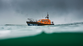 An all-weather Shannon class lifeboat is afloat on the horizon in choppy waves underneath a grey, angry sky