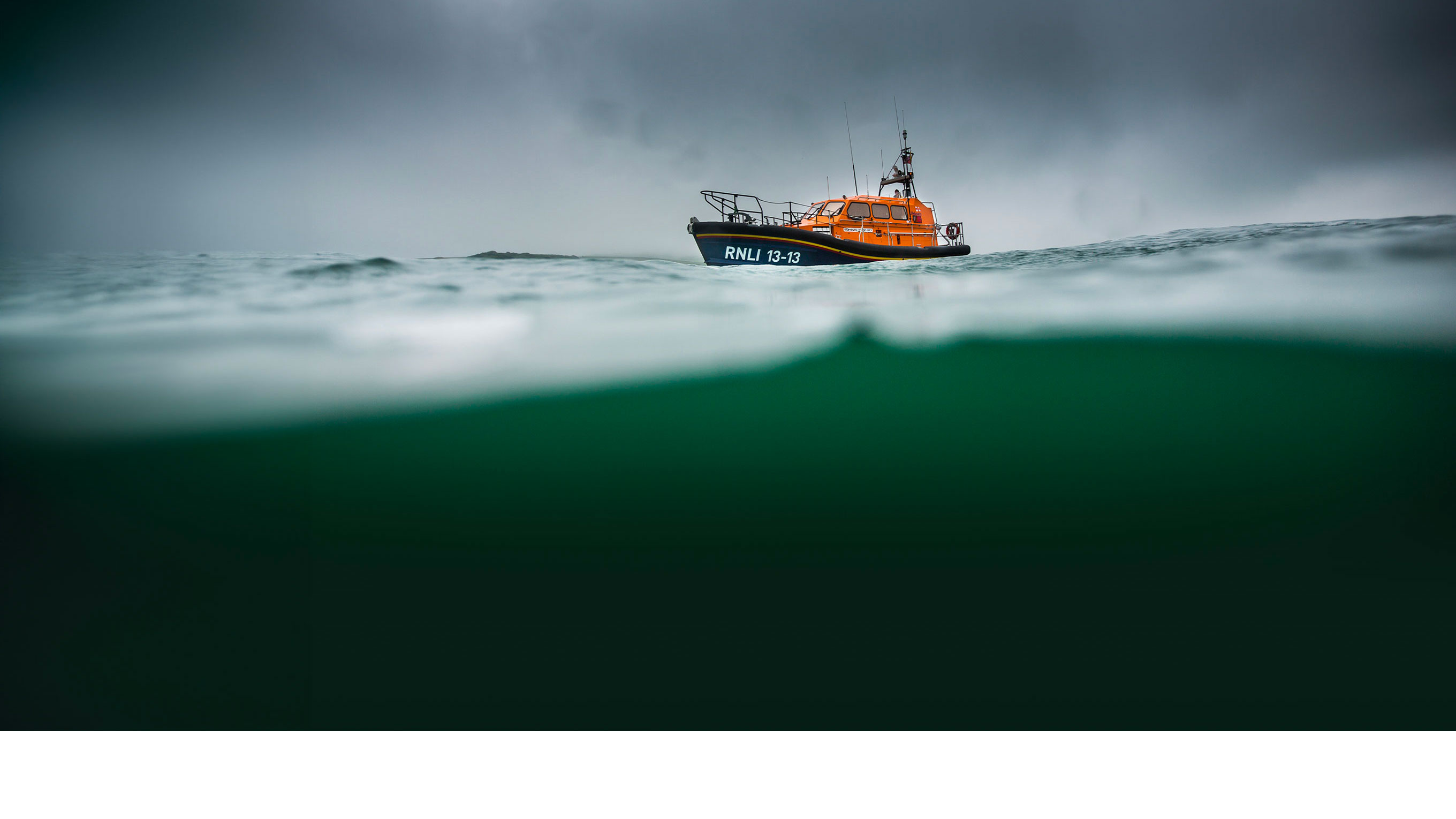 An all-weather Shannon class lifeboat is afloat on the horizon in choppy waves underneath a grey, angry sky.