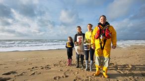 An RNLI crew member standing with three fundraisers on a sandy beach with the sea in the background