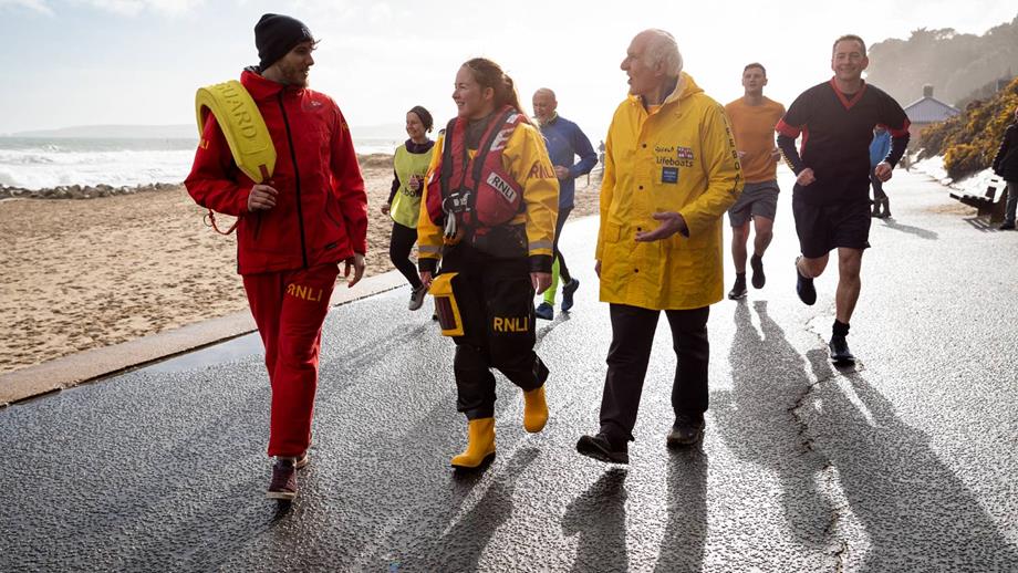 Mixed group of RNLI fundraisers walking and running on a promenade 