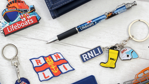 Items for sale at the RNLI shop, with RNLI logo including wallet, key chain, badge. pin, bookmark and RNLI pen