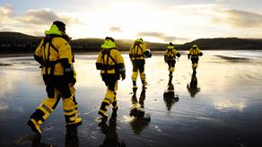 Five Girvan crew members in crew kit walking along a beach in the evening with the sun setting in the distance