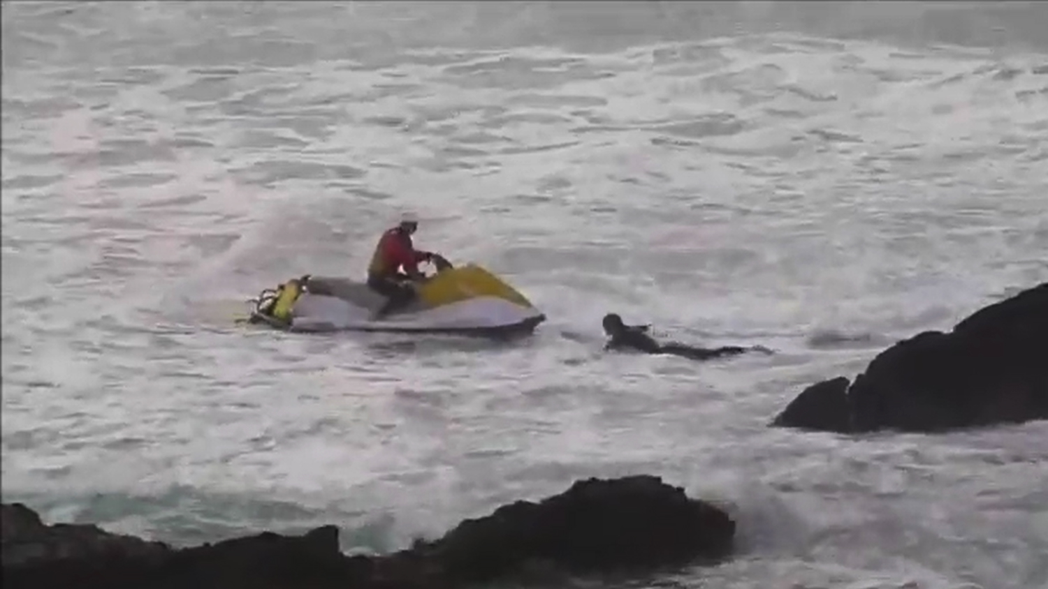 An RNLI lifeguard on a rescue watercraft goes to the rescue of a surfer in trouble