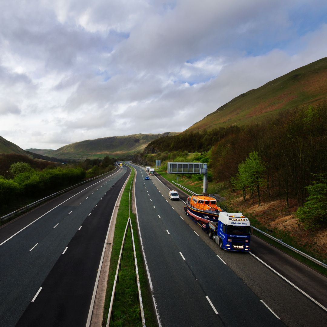 A mersey class lifeboat being transported along a motorway by lorry