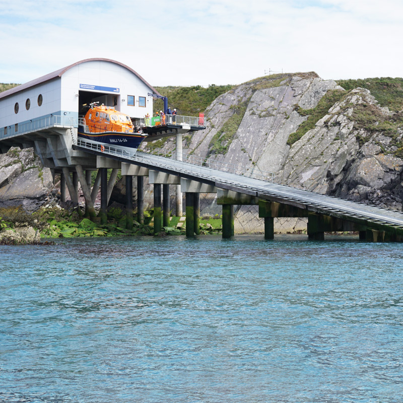 A Tamar class lifeboat emerges from a boathouse as it launches down a slipway